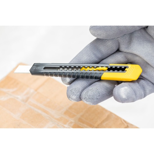 STANLEY 0-10-150 utility knife in black and yellow, held with a glove above cardboard.