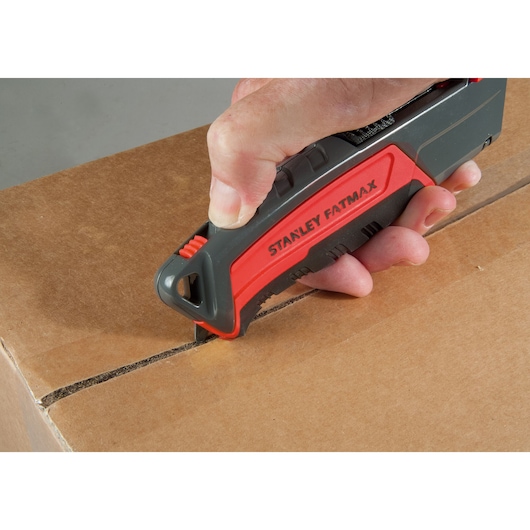 STANLEY 0-10-242 utility knife being used to cut a cardboard box, close-up of hand holding the red and black tool.
