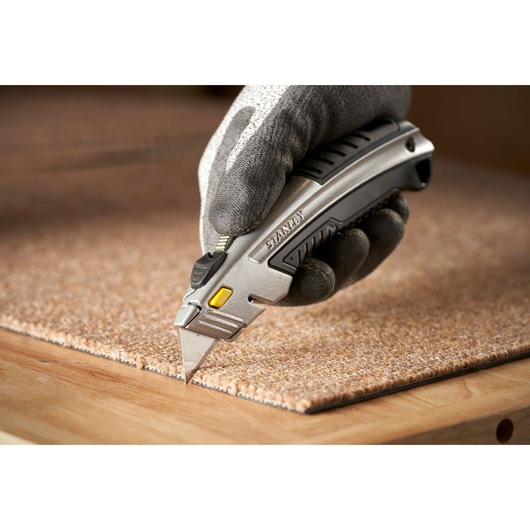 Photo of STANLEY 0-10-788 utility knife cutting carpet, held by gloved hand.