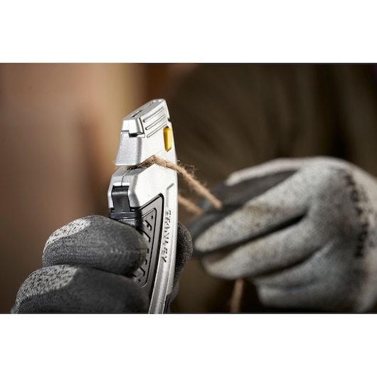 Photo of STANLEY 0-10-788 utility knife cutting twine, held in gloved hands, close-up.