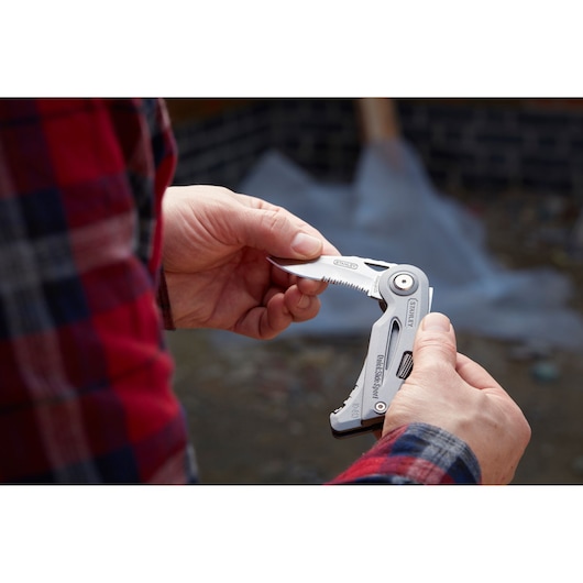 Photo of STANLEY 0-10-813 multitool knife being held outdoors, partially open showing serrated blade.