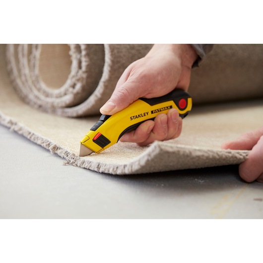 STANLEY 0-11-700 utility knife cutting carpet, close-up photo, yellow and black handle, FatMax series.
