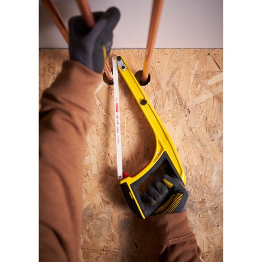 STANLEY 0-20-108 hacksaw with yellow frame cutting copper pipe, viewed from above, held by gloved hands.