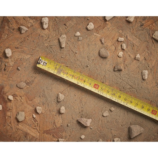 STANLEY 0-30-497 tape measure on a dusty, wooden surface with scattered small rocks, shown from above.