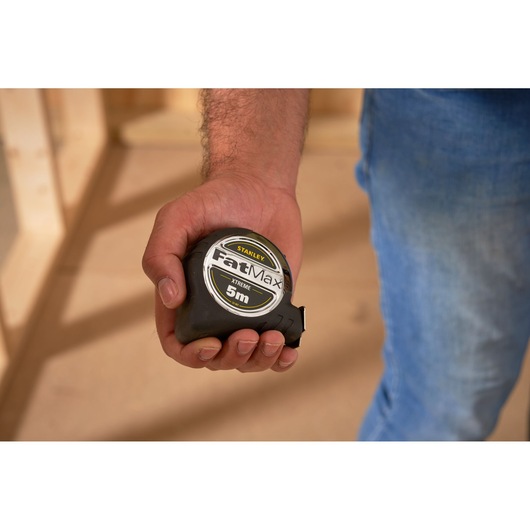 Photo of a hand holding a STANLEY 0-33-887 FatMax XTREME 5m tape measure, indoor setting.
