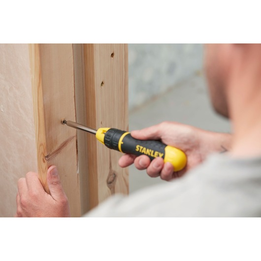 Stanley 0-68-010 screwdriver used to drive a screw into a wooden frame, close-up side view.