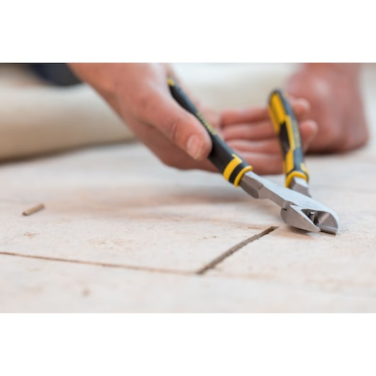 STANLEY 0-89-861 hand cutting pliers in use, black and yellow handle, close-up on tile flooring.
