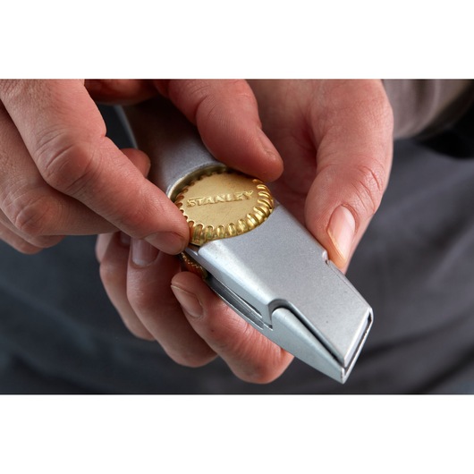 Close-up photo of hands adjusting STANLEY 1-10-550 utility knife with metallic and gold detail.