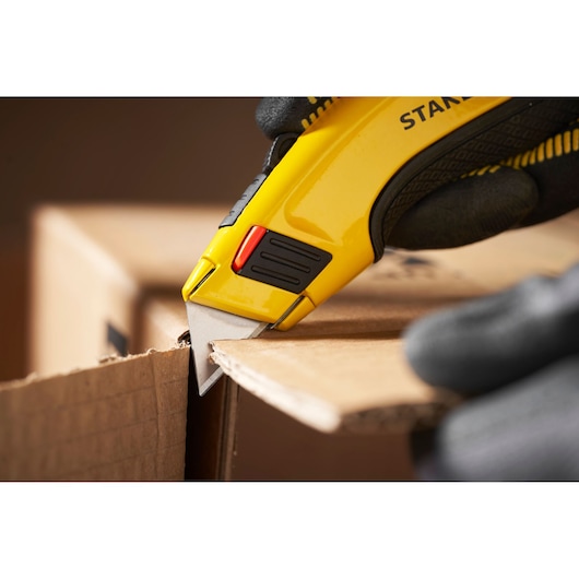 Stanley 1-11-700 utility knife cutting cardboard, close-up photography with glove holding tool.