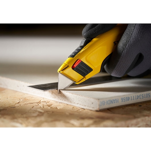 STANLEY 1-11-700 utility knife cutting drywall, close-up showing ergonomic yellow handle and gloved hand.