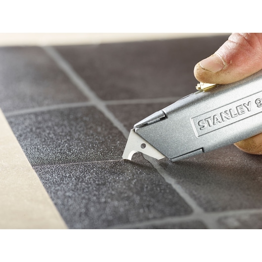 Photo of STANLEY 1-11-802 utility knife cutting black tile grout line, close-up angle.