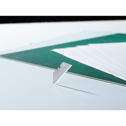 STANLEY 1-11-911 utility blade standing upright, green cutting mat and white sheets in background, side angle photo.