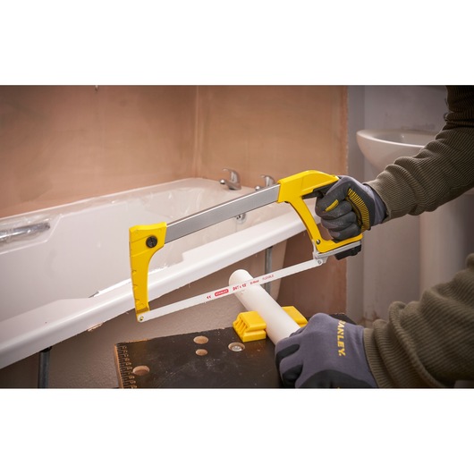 Photo of STANLEY 1-20-110 hacksaw used to cut white PVC pipe, close-up view in a bathroom setting.