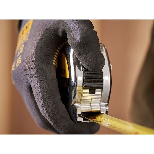 Close-up of gloved hand holding STANLEY 1-33-195 tape measure, yellow blade extended, photography.