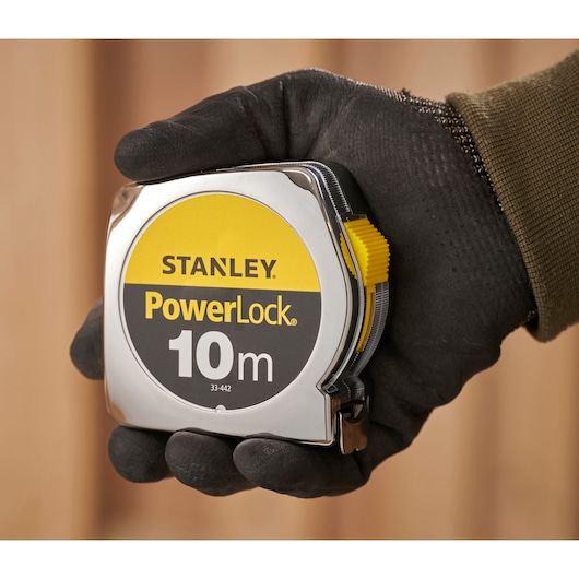 STANLEY 1-33-442 PowerLock 10m tape measure held in a gloved hand, close-up photography.