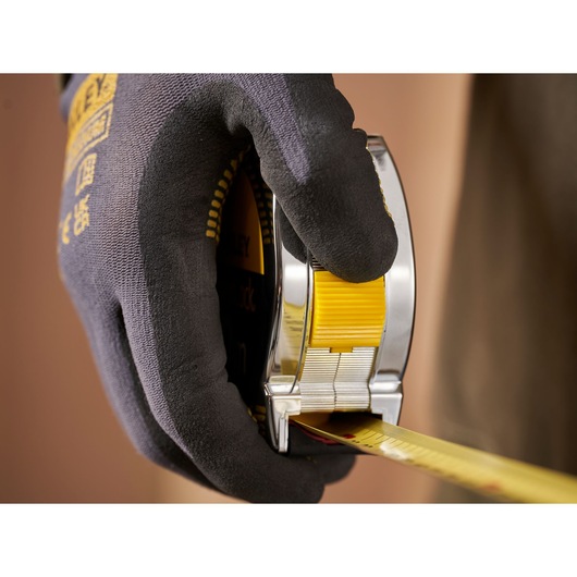Photo of a gloved hand holding a STANLEY 1-33-442 tape measure, yellow and chrome casing, extended measuring tape.