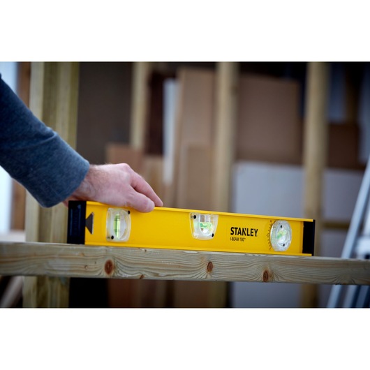STANLEY 1-42-920 spirit level in use on wooden beam, yellow body with three vials, product in action.