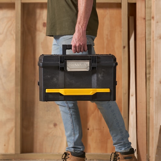 STANLEY 1-70-316 black toolbox with yellow latch, carried by hand, photography of product in use.