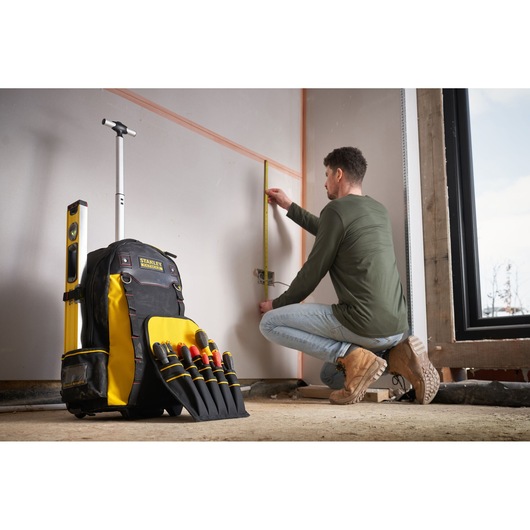 Photo of STANLEY 1-79-215 tool backpack with yellow and black color, visible hand tools, and a level, at a job site.