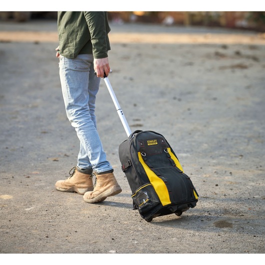 Photo of STANLEY 1-79-215 rolling tool bag with yellow and black design, extended handle, outdoors on gravel.