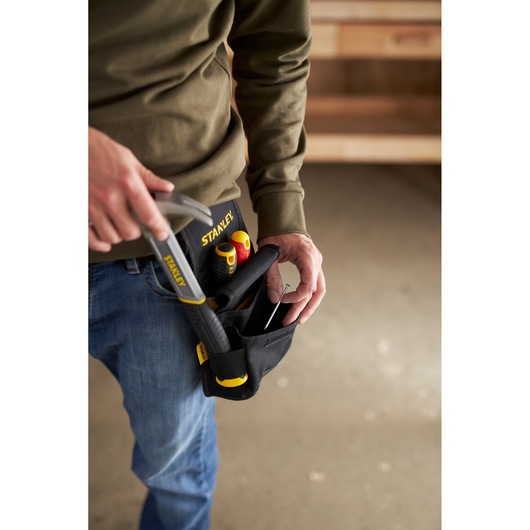 Photo of a person wearing a STANLEY tool belt pouch SKU 1-93-329 holding hand tools, indoor workshop setting.