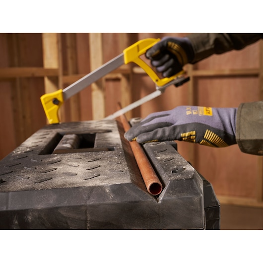 STANLEY 1-95-615 hacksaw cutting copper pipe on workbench, close-up angle, worker wearing gloves.