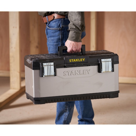 Photo of STANLEY 1-95-616 toolbox with black handle, silver latches, carried by person in construction setting.