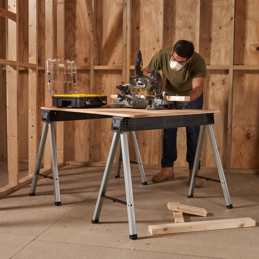 Photo of STANLEY 1-97-475 metal sawhorses used as a workbench in a wooden frame construction site.