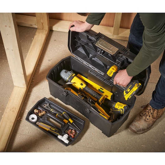 STANLEY 1-97-510 toolbox with open lid showing assorted hand tools, drill, and accessories on workshop floor, top angle.