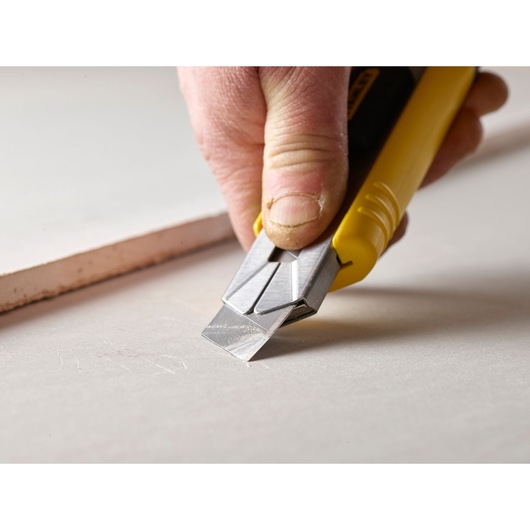 Photo of STANLEY 2-11-725 utility knife cutting drywall sheet close-up, showing yellow handle and metal blade.