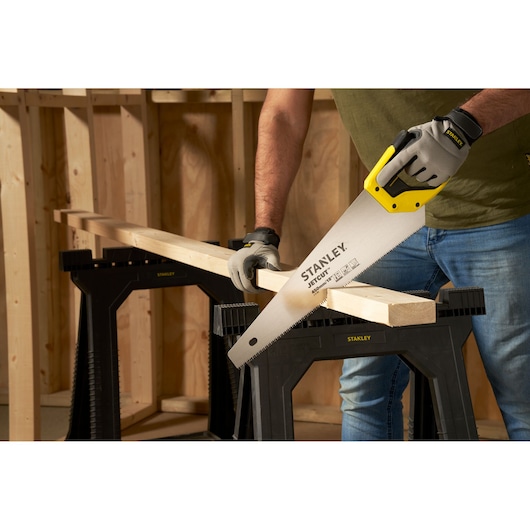 STANLEY 2-15-283 hand saw cutting wood on black sawhorse in workshop, close-up angle.