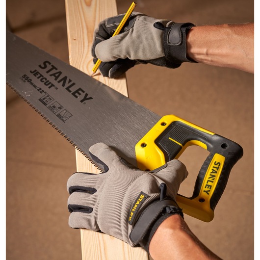 STANLEY 2-15-289 hand saw with yellow and black handle cutting wood, worker wearing gray gloves, close-up.