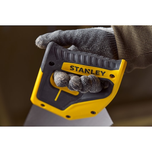Photo of a gloved hand gripping STANLEY 2-20-037 saw handle, close-up on yellow and black ergonomic grip.