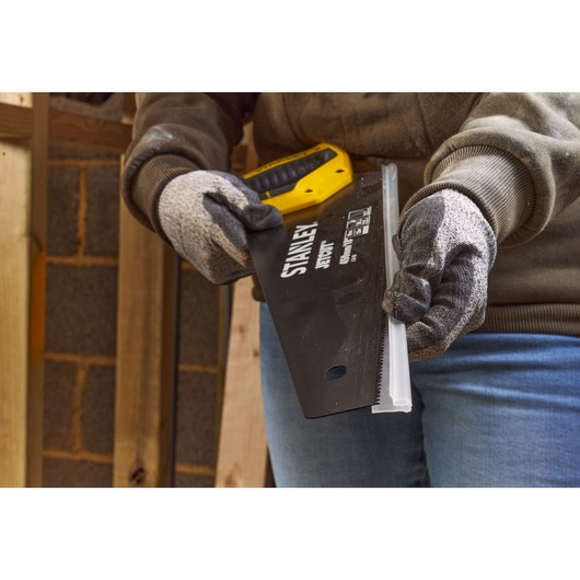 STANLEY 2-20-180 hand saw with yellow and black handle held by gloved hands in workshop setting.