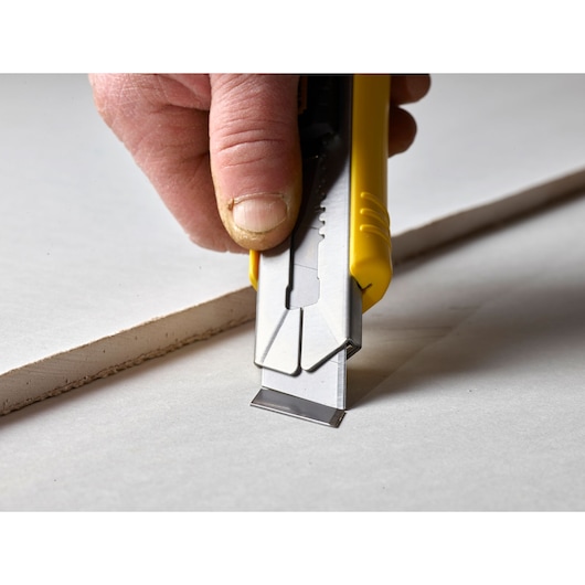 STANLEY 3-11-725 utility knife with yellow handle cutting drywall, close-up side view.