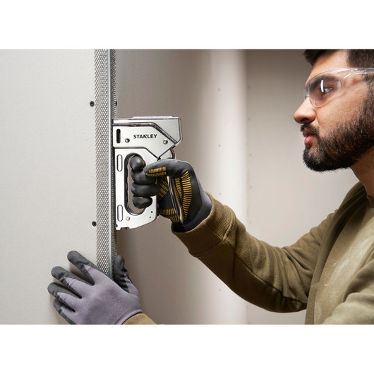 Stanley 6-TR110 heavy-duty staple gun used on drywall, close-up of gloved hands during construction task.