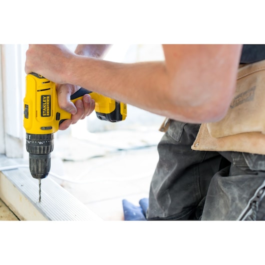 Photo of STANLEY FMC011S2 cordless drill in use, yellow body, close-up side angle.