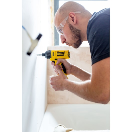 Stanley FMC041S2 cordless drill used on a wall, close-up view showing yellow and black tool in action.