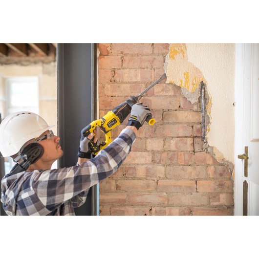 STANLEY FMCD900M2S demolition hammer used to remove plaster from brick wall in construction setting.