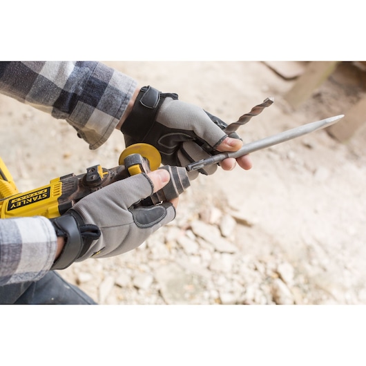 Photo of STANLEY FMCD900M2S grinder held in gloved hands sharpening a metal tool outdoors.