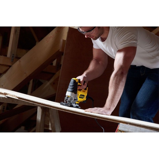 STANLEY FME340K jigsaw tool cutting wood plank, handheld, in workshop setting.