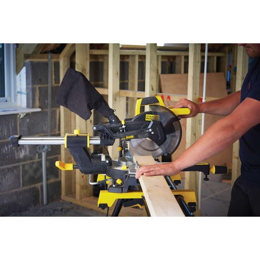 STANLEY FME721 miter saw cutting wood in a workshop, side view with visible dust bag and yellow details.