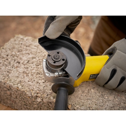 Photo of STANLEY FMEG225VS angle grinder being held with gloves, close-up on tool head, outdoors.