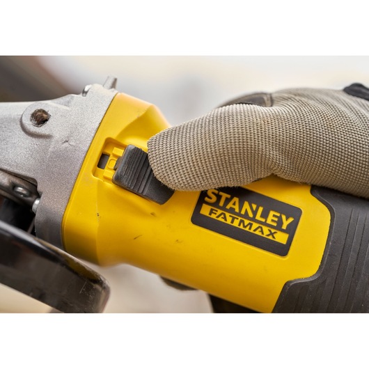 STANLEY FMEG225VS angle grinder close-up with gloved hand pressing power switch, yellow and black body.