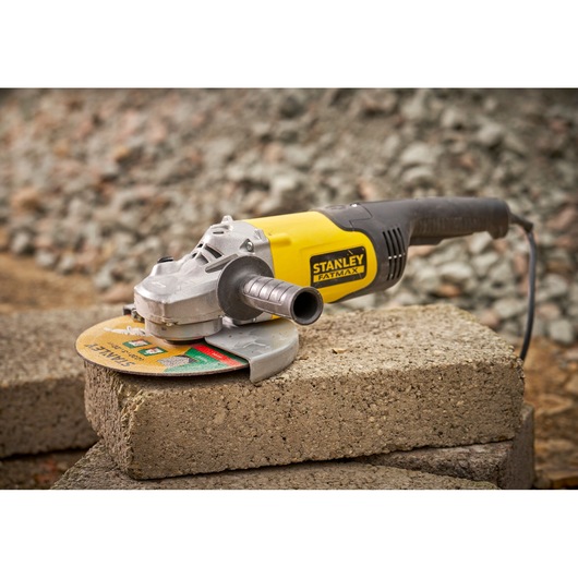 STANLEY FMEG232 angle grinder with yellow and black body, shown on concrete blocks, side view.