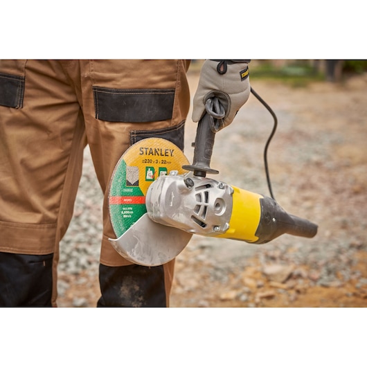 Stanley FMEG232 angle grinder held by gloved hand outdoors, yellow and black body, circular cutting disc.