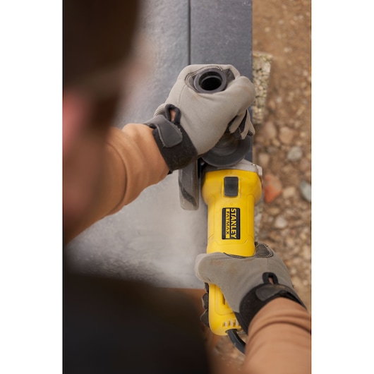 Photo of STANLEY FMEG615 angle grinder in use, worker wearing gloves, grinding metal surface.