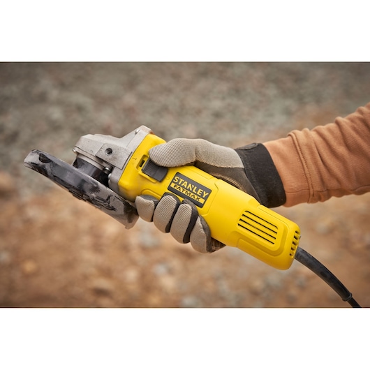Stanley FMEG615 angle grinder held in a gloved hand, yellow body, outdoors, product category photography.