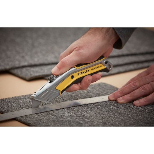 Photo of STANLEY FATMAX FMHT0-10288 utility knife cutting carpet along a metal ruler.