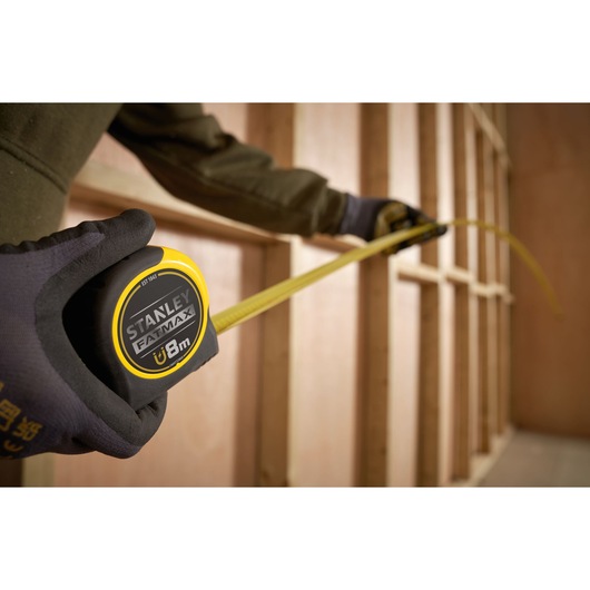 Stanley FMHT0-33868 tape measure with yellow blade extended in a construction framing setting.
